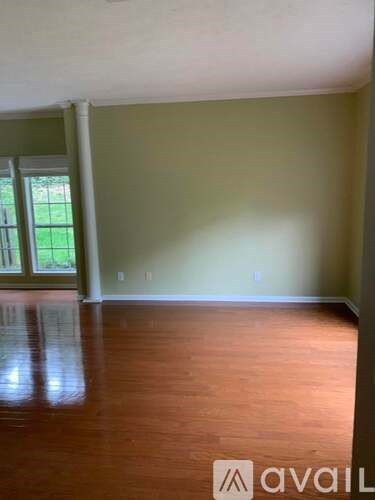 A room with wooden floors and a window overlooking a green lawn.