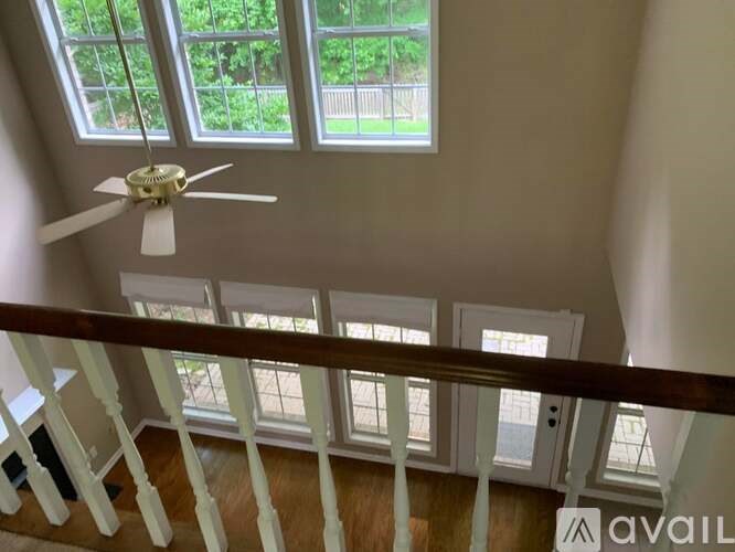 A room with a ceiling fan and a view of a garden through the windows.