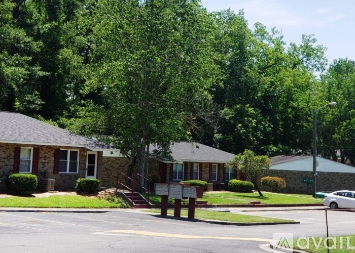 A small building with a red brick exterior is surrounded by green trees.