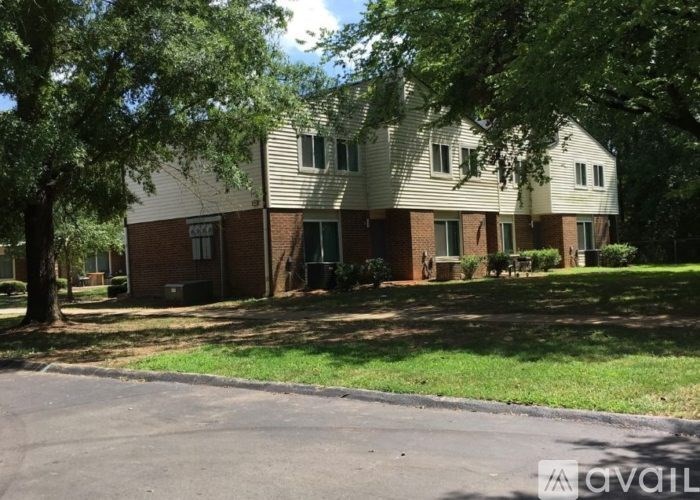 A house with a brown brick base and a white siding upper part surrounded by green trees.