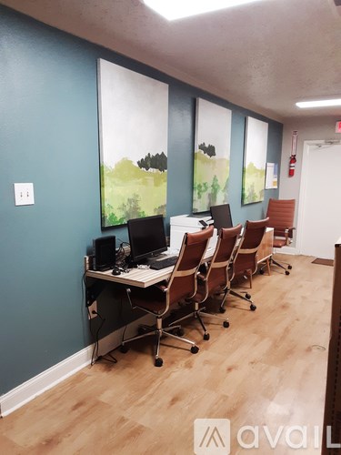 A row of chairs are lined up in front of a desk with a laptop and a monitor on it.