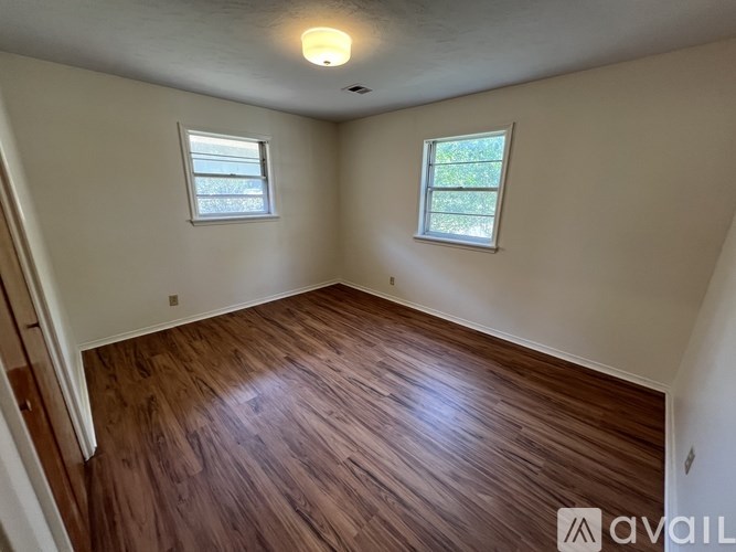 A room with wooden flooring and two windows.