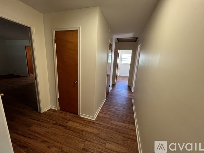 A hallway with wooden floors and white walls leading to a door.