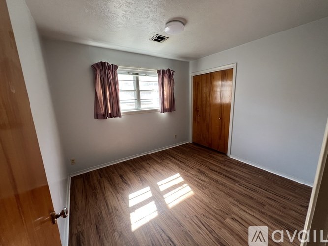 A room with wooden flooring and a window with red curtains.