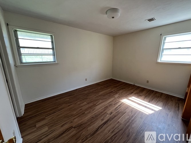 A room with wooden flooring and two windows.
