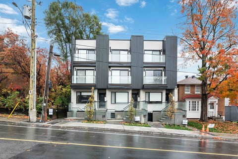 A modern building with a grey facade is situated on a street with trees showing autumn colors.