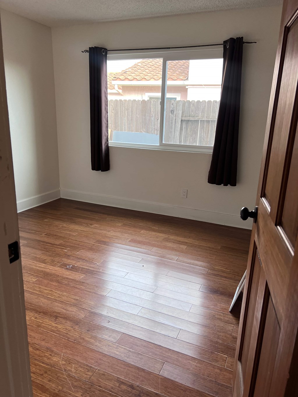 A room with wooden floors and a window with black curtains.