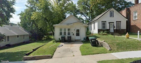 A small white house with a black door and windows is surrounded by a green lawn.