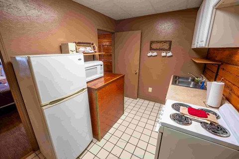 A kitchen with a white refrigerator, a stove with a red pot on it, and a brown counter.