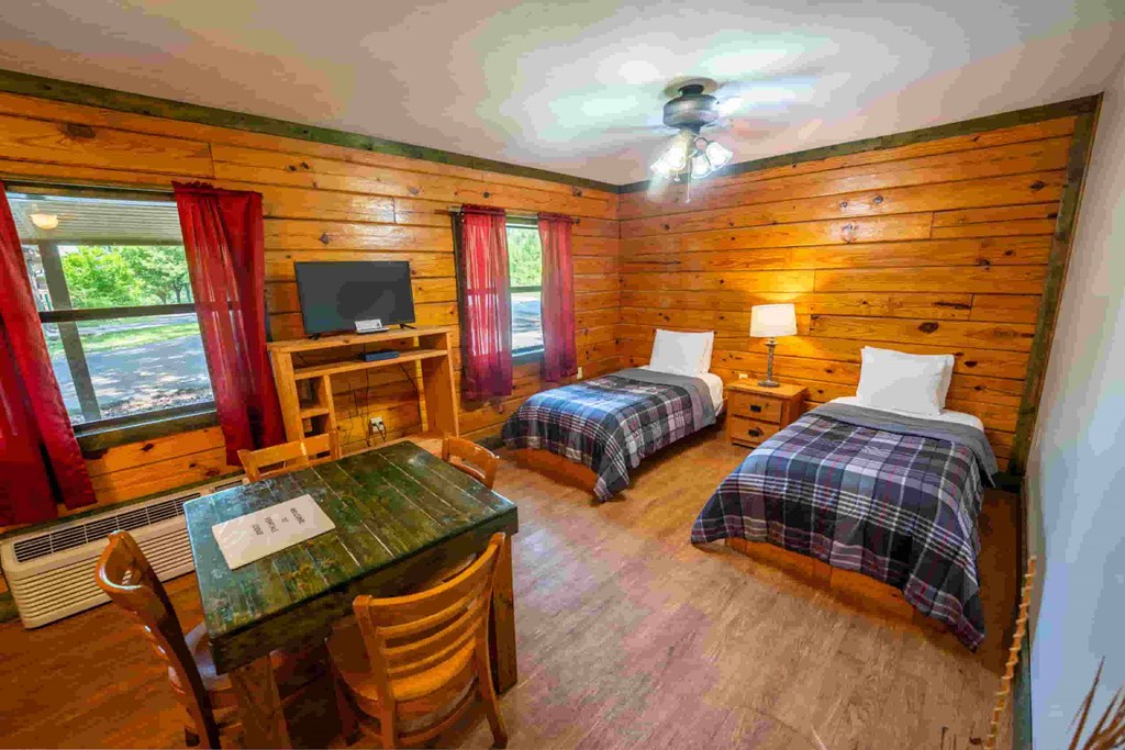 A cozy room with a wooden ceiling and walls, two twin beds, a table, chairs, and a television.