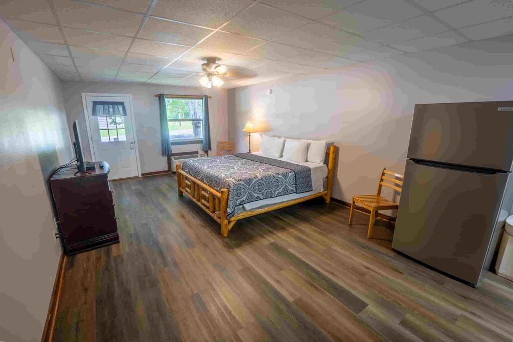 A bedroom with a bed, chair, and refrigerator.