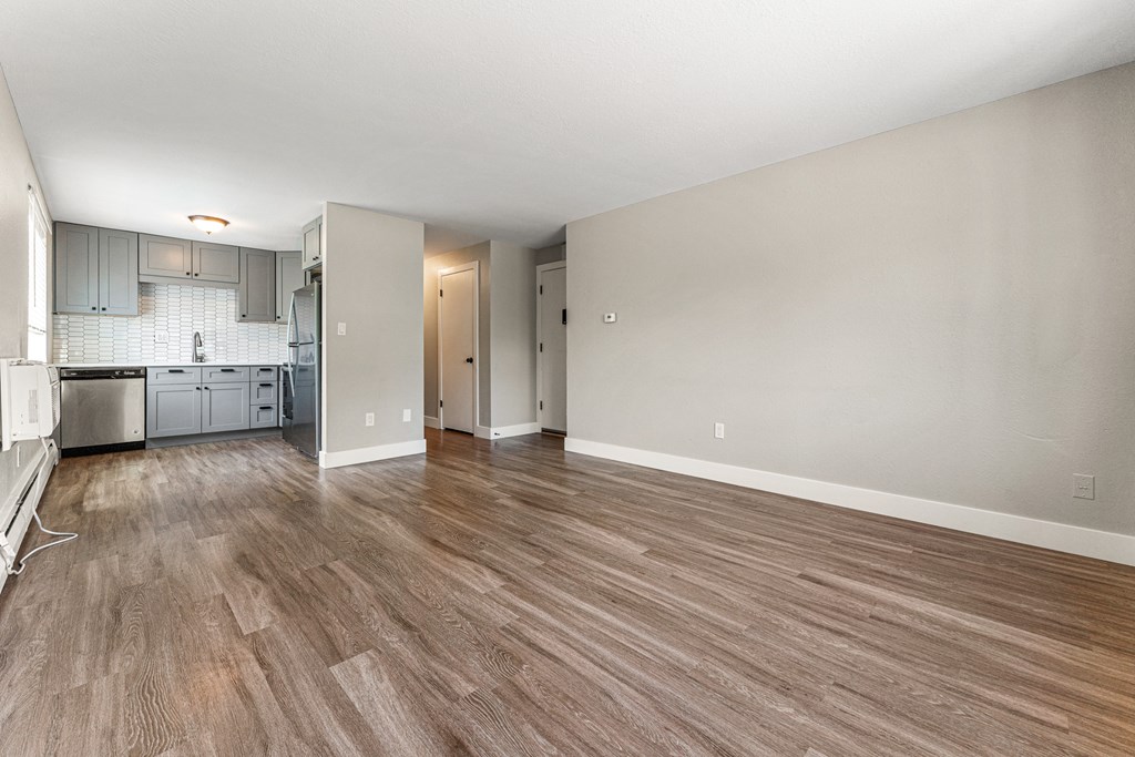 A room with wooden flooring and a kitchen area in the background.