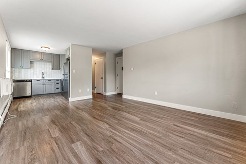 A room with wooden flooring and a kitchen area in the background.