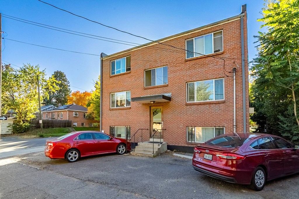 Two red cars parked in front of a brick building.