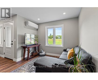 A living room with a grey couch and a window showing a view of a field.