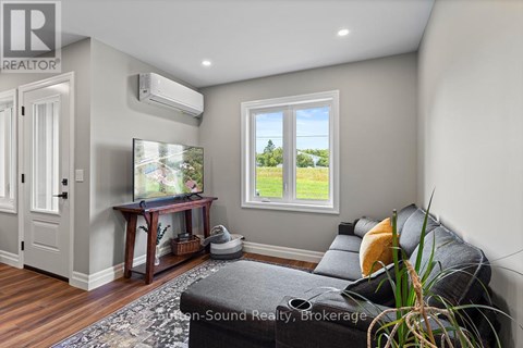 A living room with a grey couch and a window showing a view of a field.
