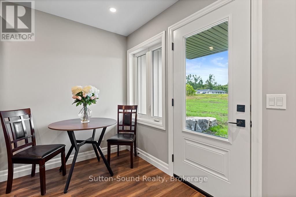 A dining room with a table and chairs and a view of a green field through the door.