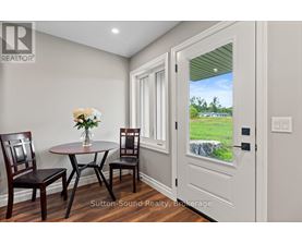 A dining room with a table and chairs and a view of a green field through the door.