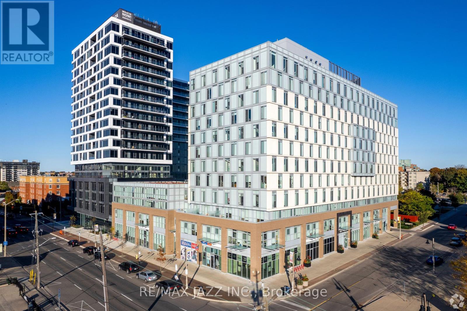 A modern building with a glass facade is situated next to a taller building with a brown facade.