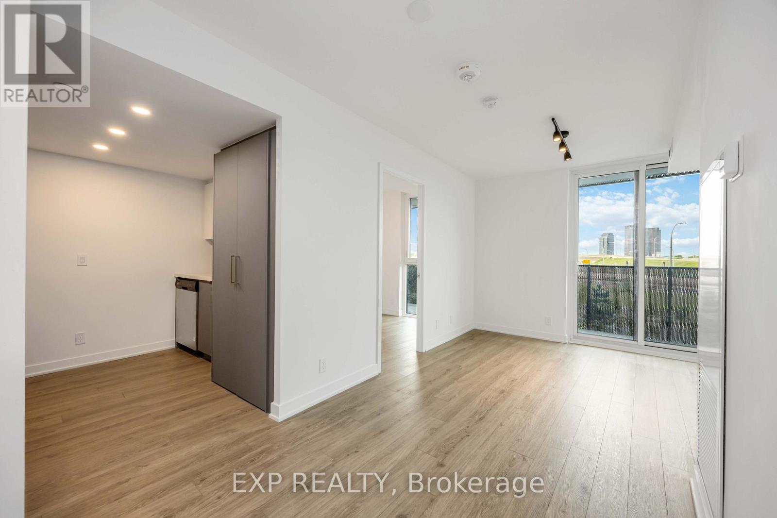A spacious room with wooden flooring and a large window overlooking a fence.