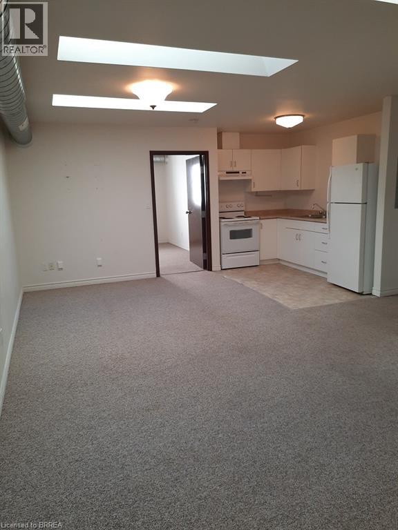 A room with a carpeted floor and a kitchen area in the background.