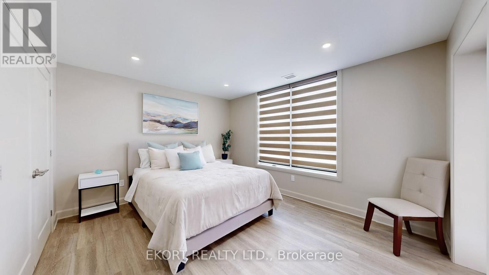 A bedroom with a large bed, a nightstand, a chair, and a painting on the wall.