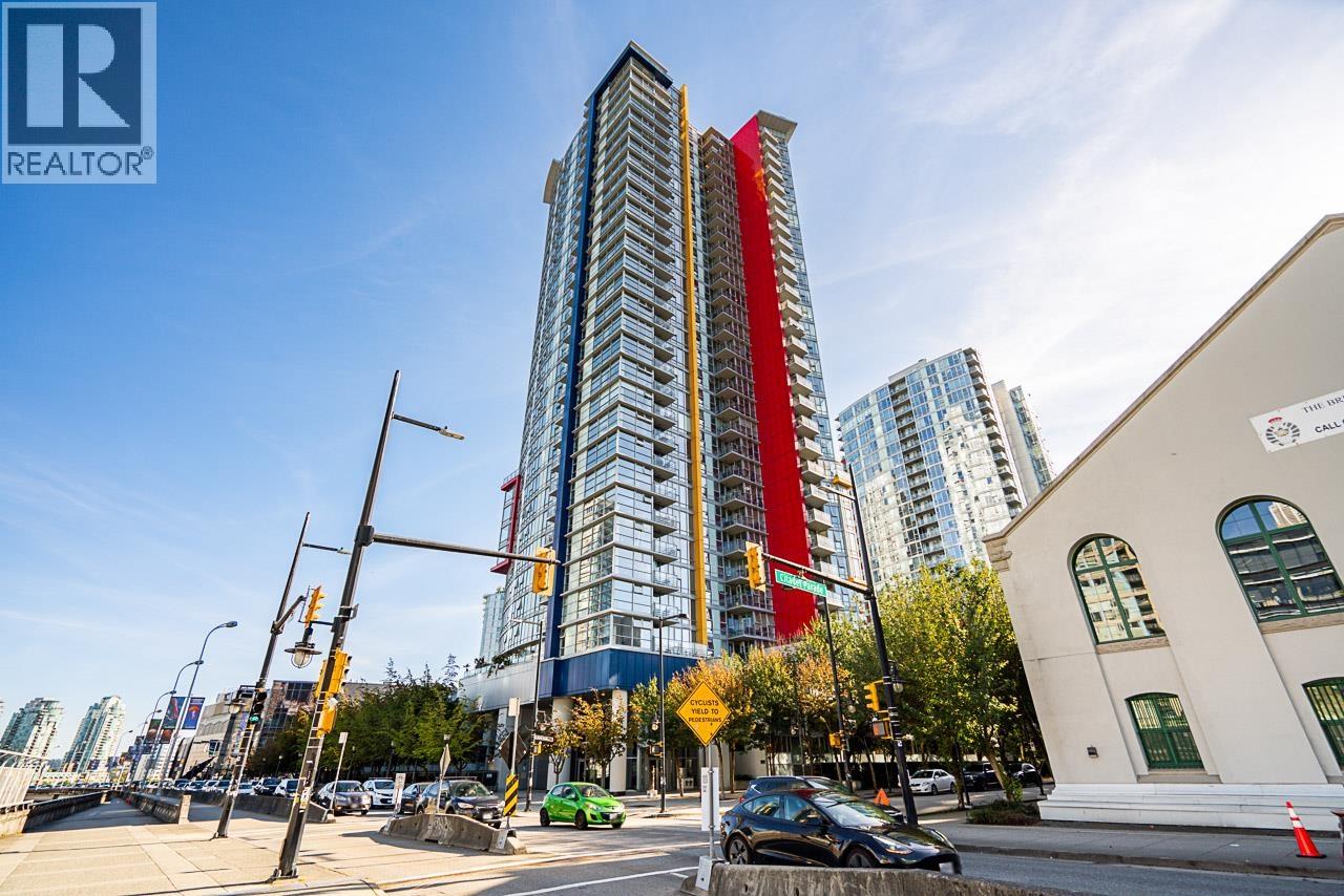 A tall building with a red stripe down the middle stands in front of a white building with a green car parked in front of it.