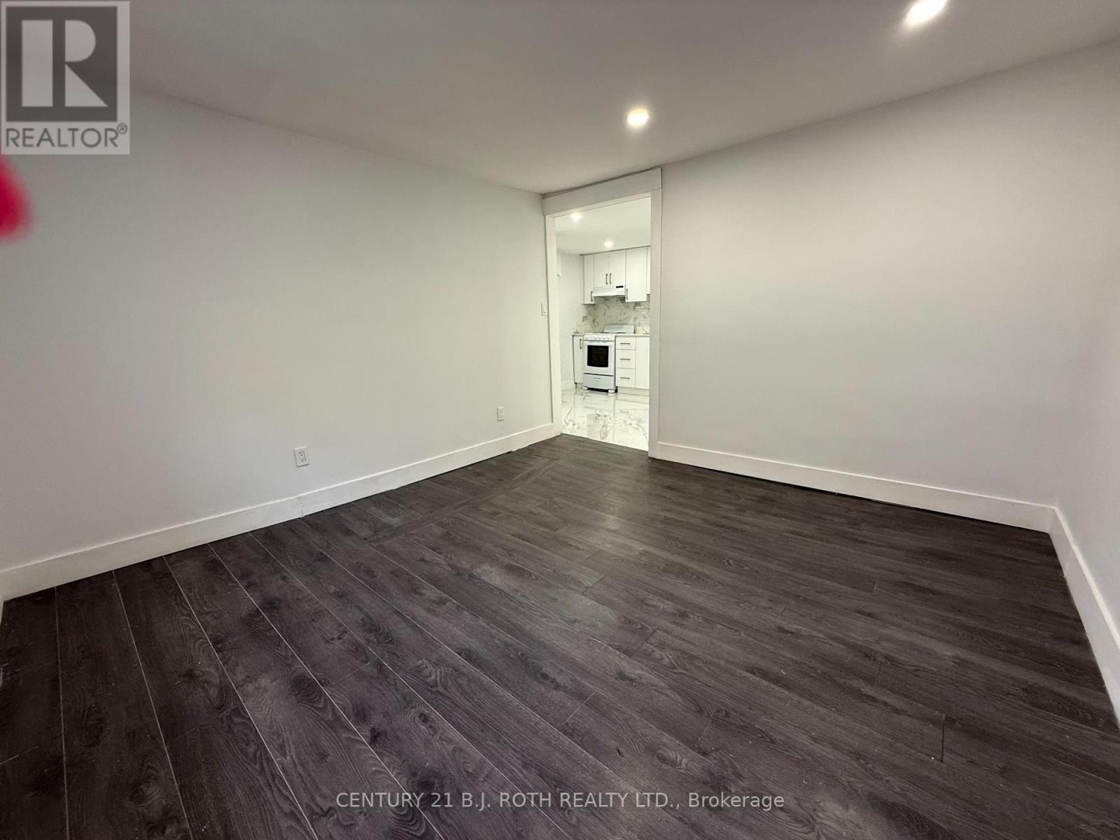 A spacious room with wooden flooring and a white wall.