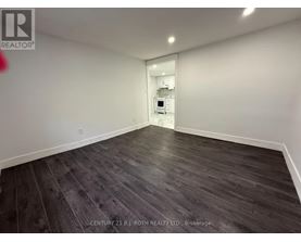 A spacious room with wooden flooring and a white wall.