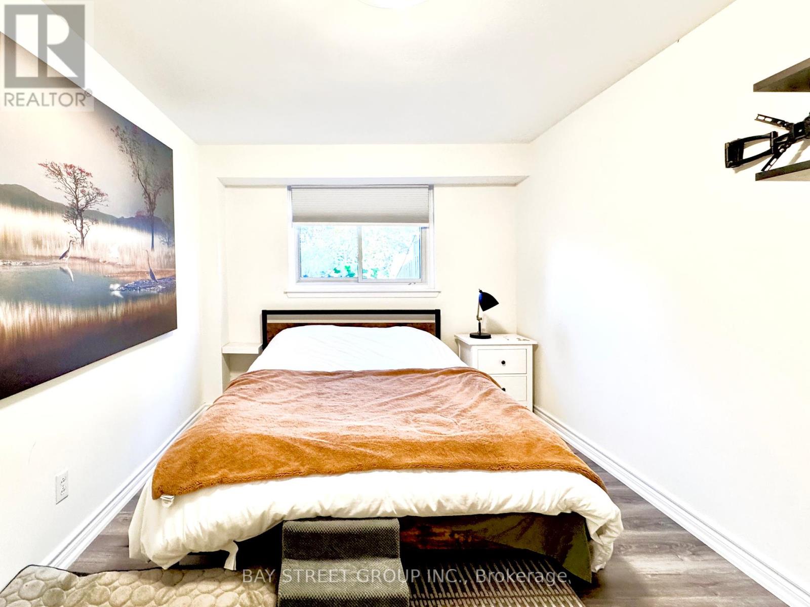 A bedroom with a bed, nightstand, and a painting on the wall.