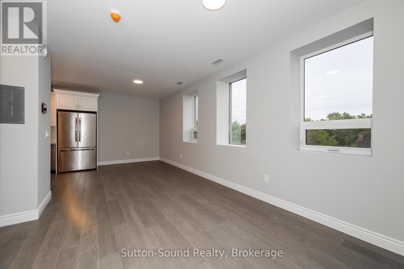 A spacious room with a stainless steel refrigerator and wooden flooring.
