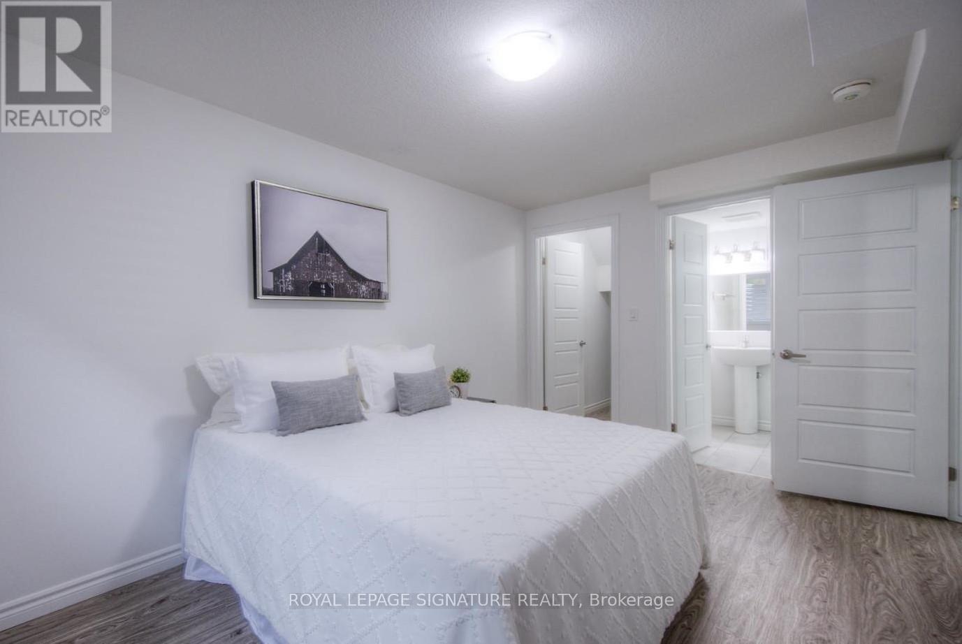 A bedroom with a bed, a picture on the wall, and a door leading to another room.