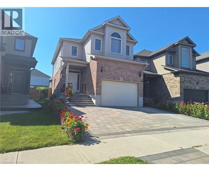 A house with a driveway and garage is surrounded by a well-kept lawn and flower beds.