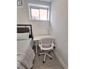 A white chair is in a white bedroom with a bed and a desk.