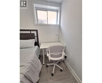A white chair is in a white bedroom with a bed and a desk.