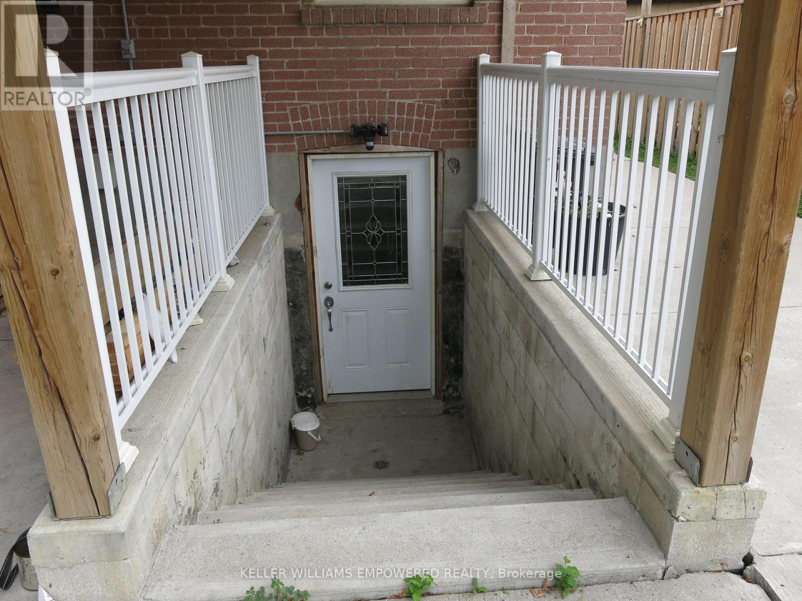 A white door with a glass window is in the middle of a concrete area with a wooden railing on either side.