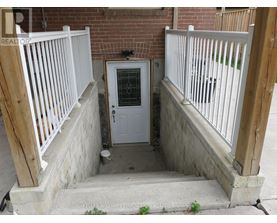 A white door with a glass window is in the middle of a concrete area with a wooden railing on either side.