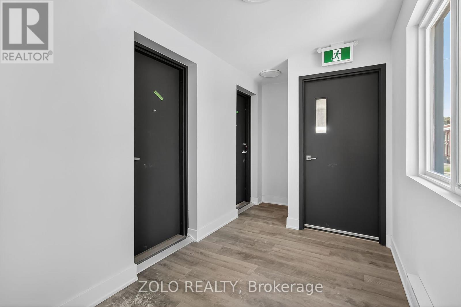 A hallway with two doors and a green exit sign above the right door.
