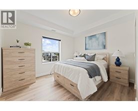 A bedroom with a large bed, a dresser, and a window overlooking a parking lot.