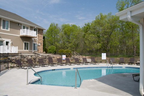 A swimming pool surrounded by chairs and trees.