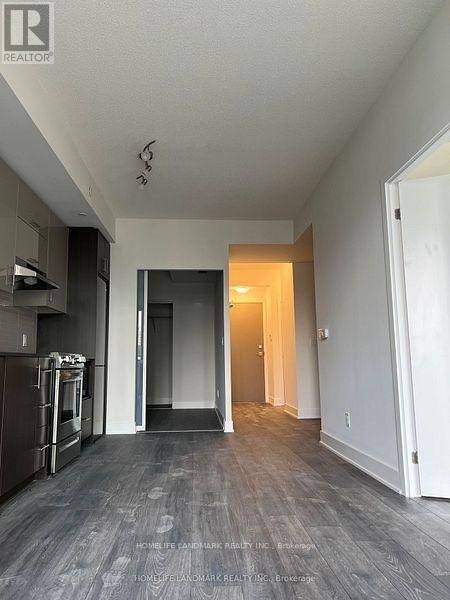 A spacious, empty room with a kitchen area to the left and a doorway leading to another room.