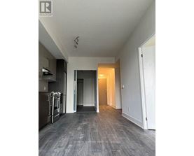 A spacious, empty room with a kitchen area to the left and a doorway leading to another room.