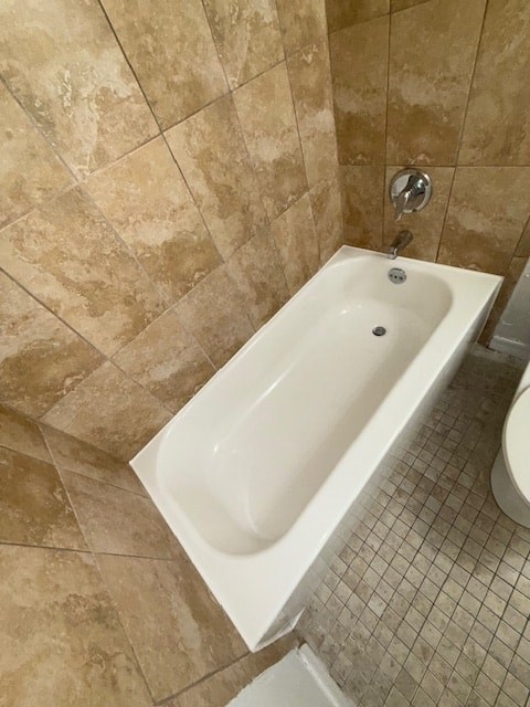 A white bathtub in a bathroom with tiled walls and floor.