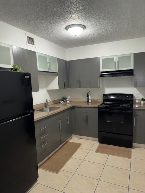 A black refrigerator is in a kitchen with grey cabinets.