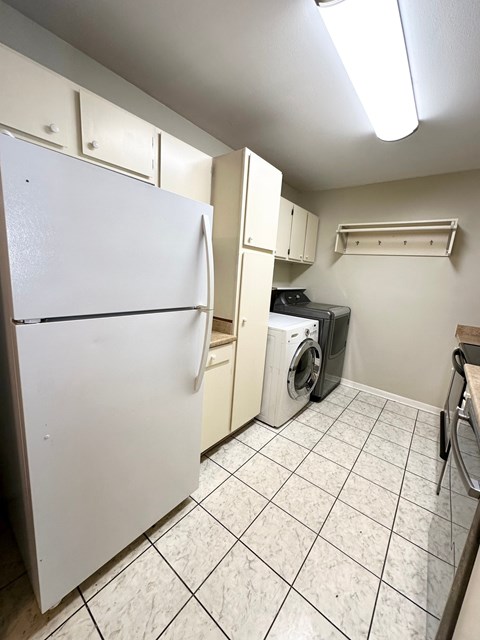 A white refrigerator is in a kitchen with white cabinets and a white washer and dryer.