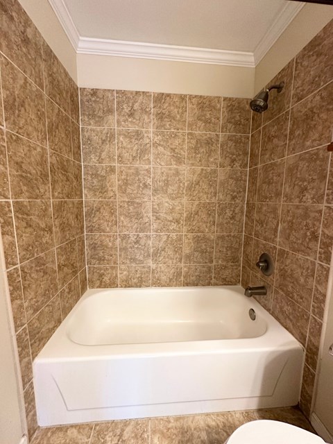 A white bathtub sits in a bathroom with brown tiled walls.
