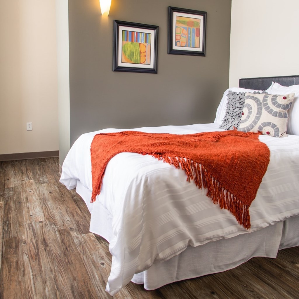 A bed with a white comforter and a red throw blanket.