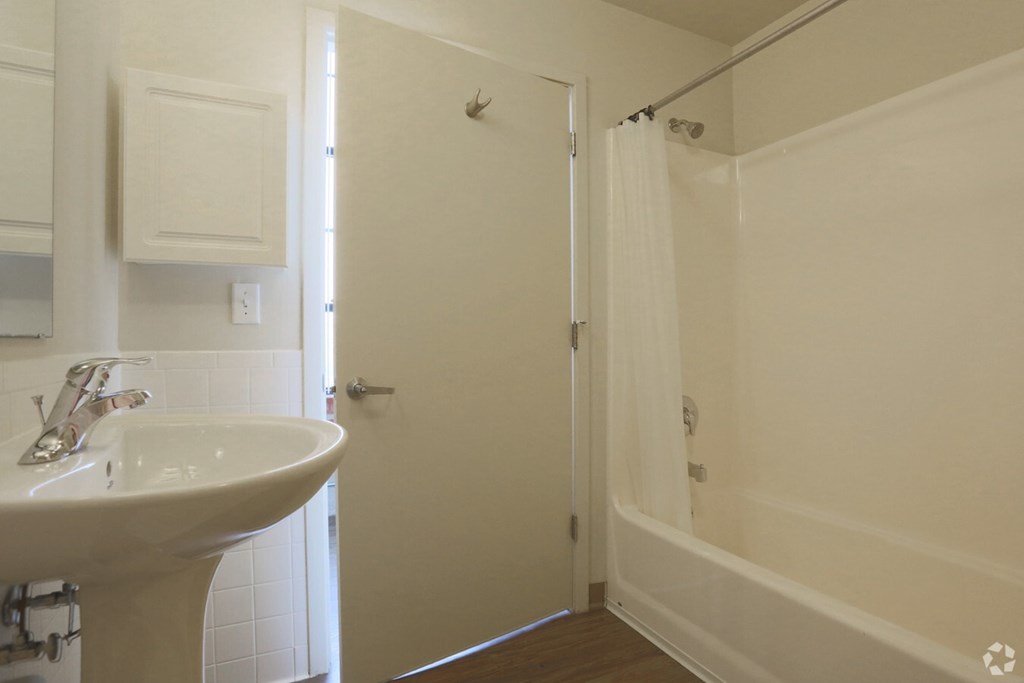 A white bathroom with a sink, mirror, and shower.