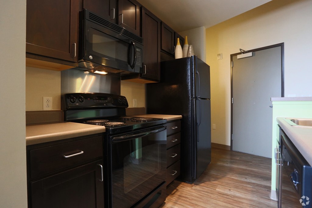 A kitchen with black appliances and wooden floors.