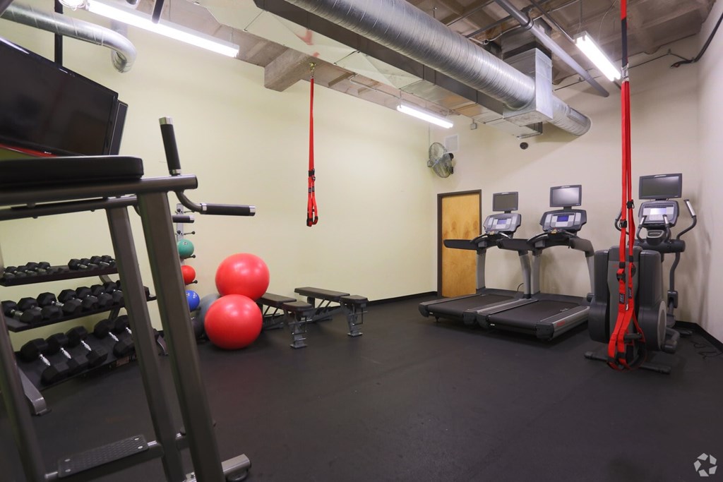 A gym with a red pull up bar, a bench, a treadmill, a weight rack and a rowing machine.